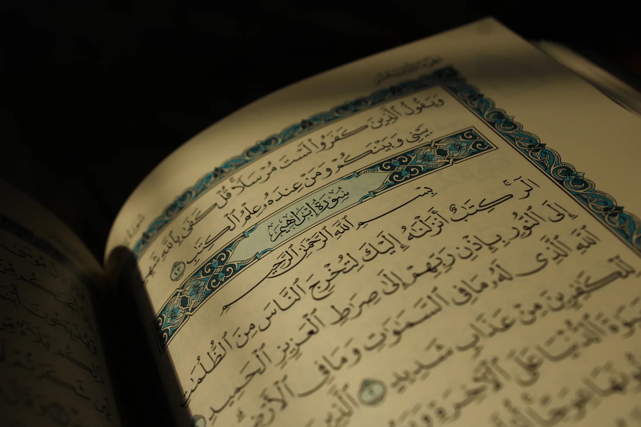 An open Qur'an, its illuminated chapter heading lit against a dark background.